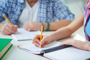 Hand of student with pencil carrying out written task or writing lecture